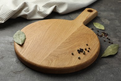 Photo of Cutting board, pepper and bay leaves on grey table. Space for text