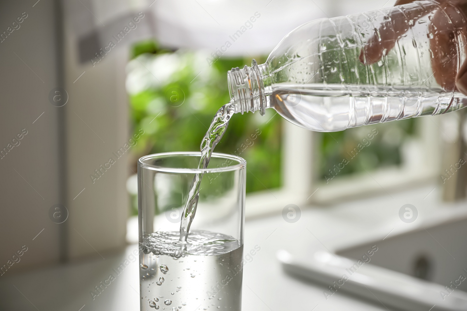 Photo of Person pouring water from bottle into glass in kitchen, closeup