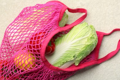 Photo of Fresh Chinese cabbage and other products in string bag on light textured table, closeup