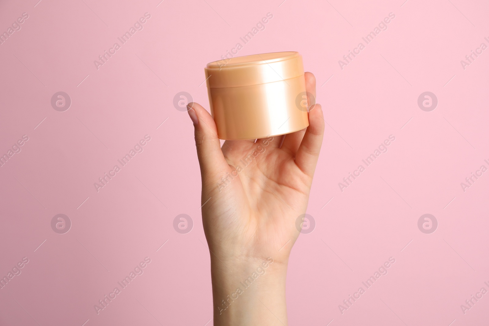 Photo of Woman holding jar of face cream on pink background, closeup