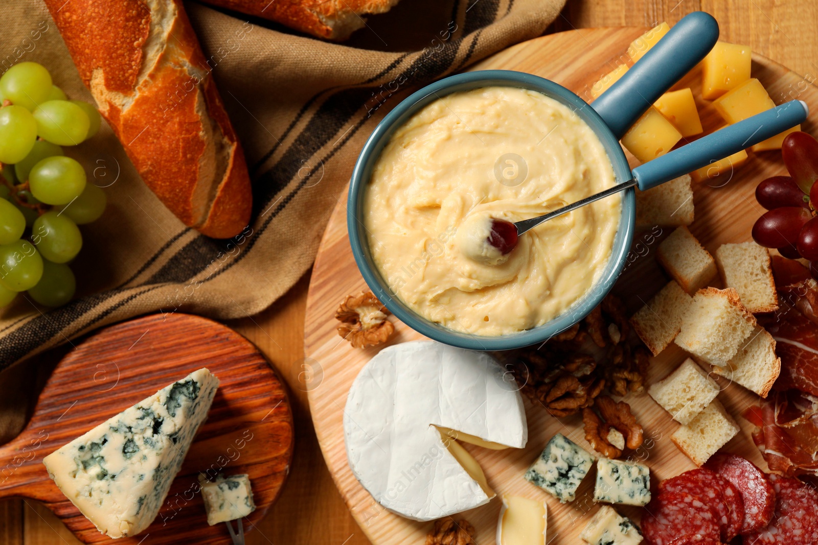 Photo of Fondue pot with tasty melted cheese, fork and different snacks on wooden table, top view