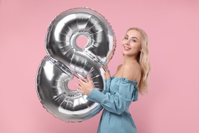 Photo of Happy Women's Day. Charming lady holding balloon in shape of number 8 on dusty pink background