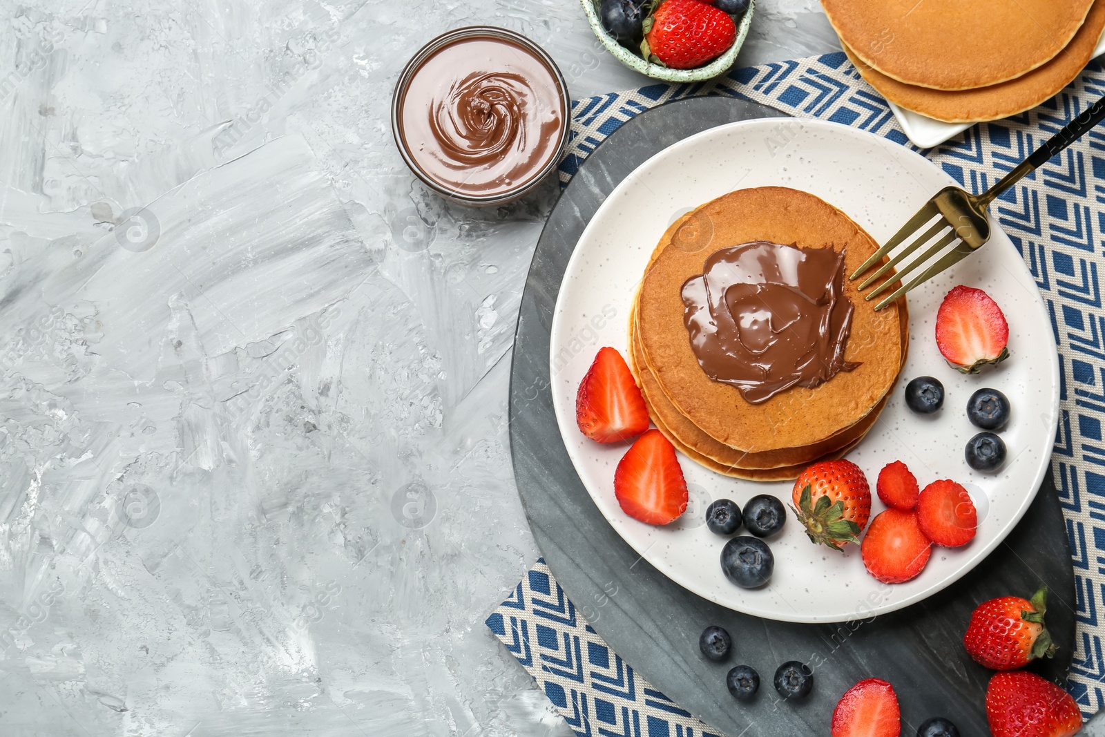 Photo of Tasty pancakes with chocolate paste and berries served on grey table, flat lay. Space for text