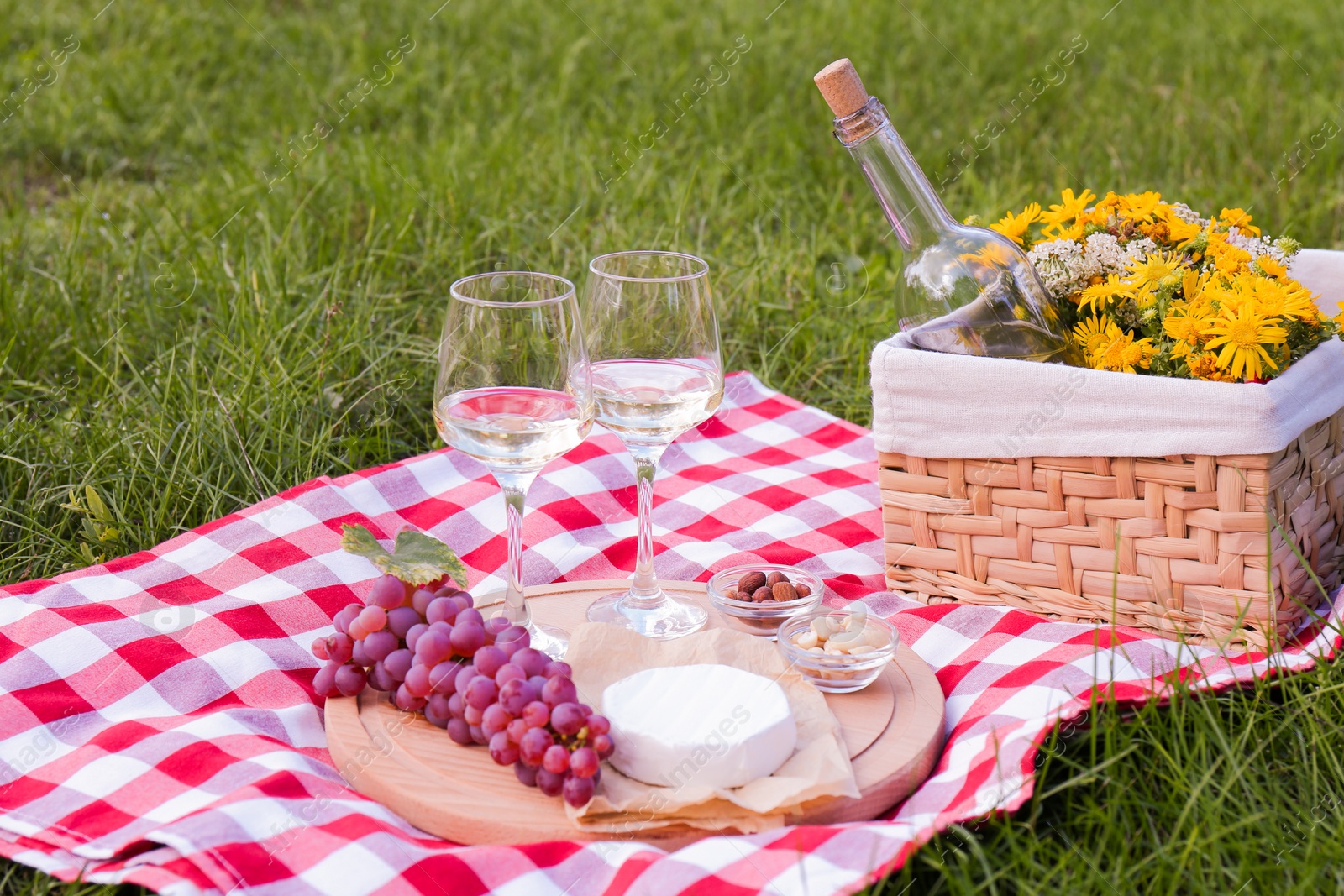 Photo of Glasses of white wine and snacks for picnic served on blanket outdoors