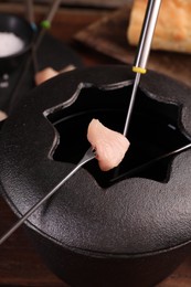 Photo of Fondue pot, forks and piece of raw meat on table, closeup