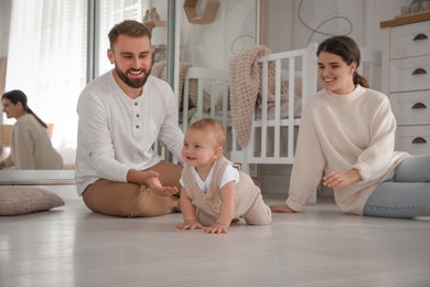 Happy parents watching their baby crawl on floor at home