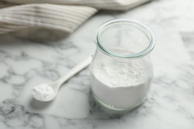 Photo of Baking powder in jar and spoon on white marble table, closeup. Space for text