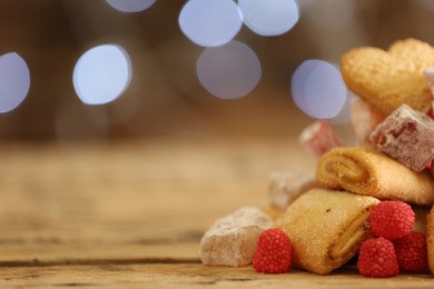 Delicious cookies and candies on wooden table against blurred background, closeup. Space for text