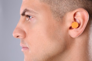 Photo of Man wearing foam ear plug on grey background, closeup