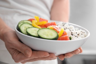 Photo of Woman holding delicious poke bowl with rice, salmon and vegetables on blurred background, closeup