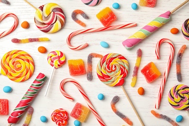 Photo of Many different yummy candies on white wooden background, top view