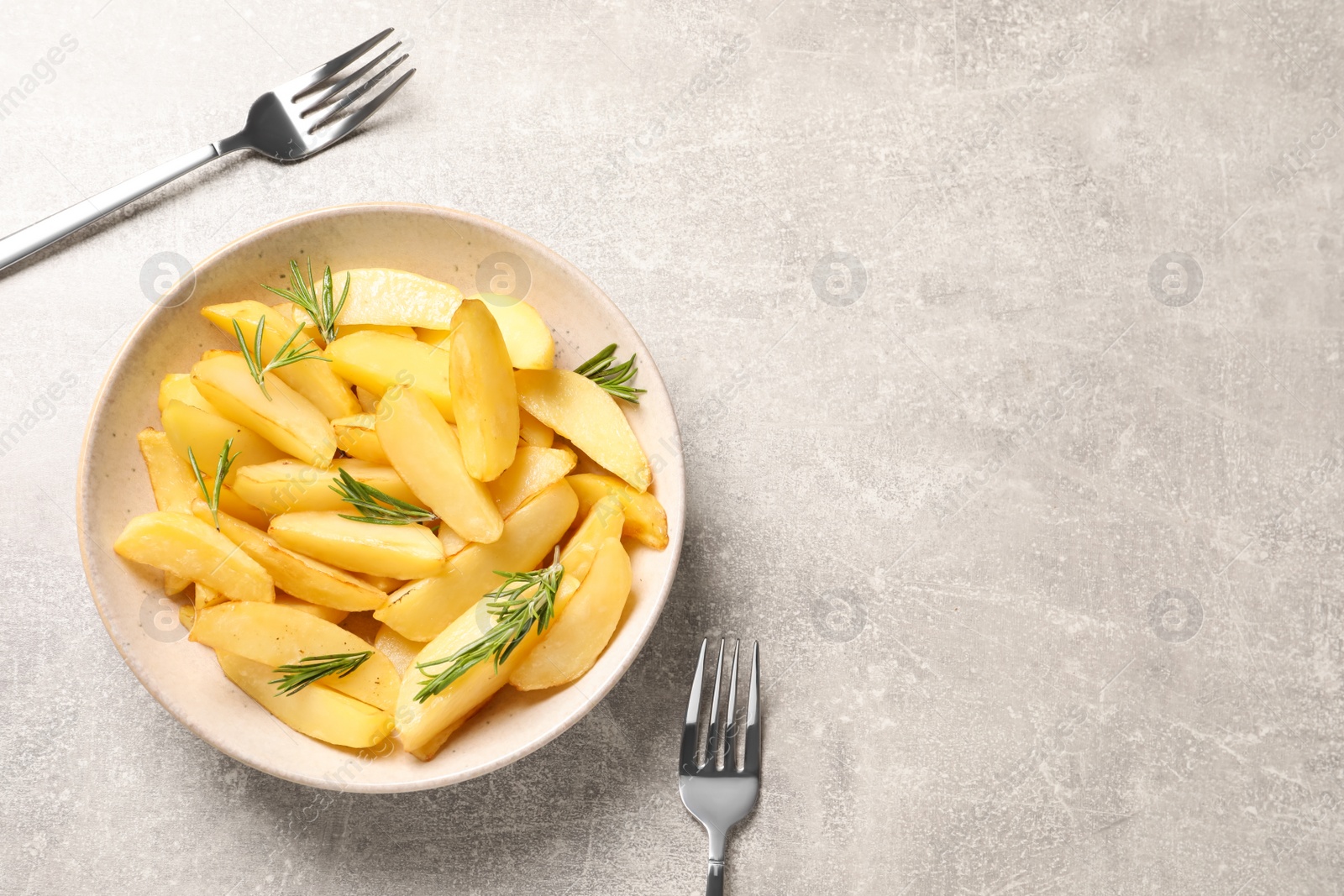 Photo of Plate with tasty baked potato wedges and rosemary on grey table, flat lay. Space for text