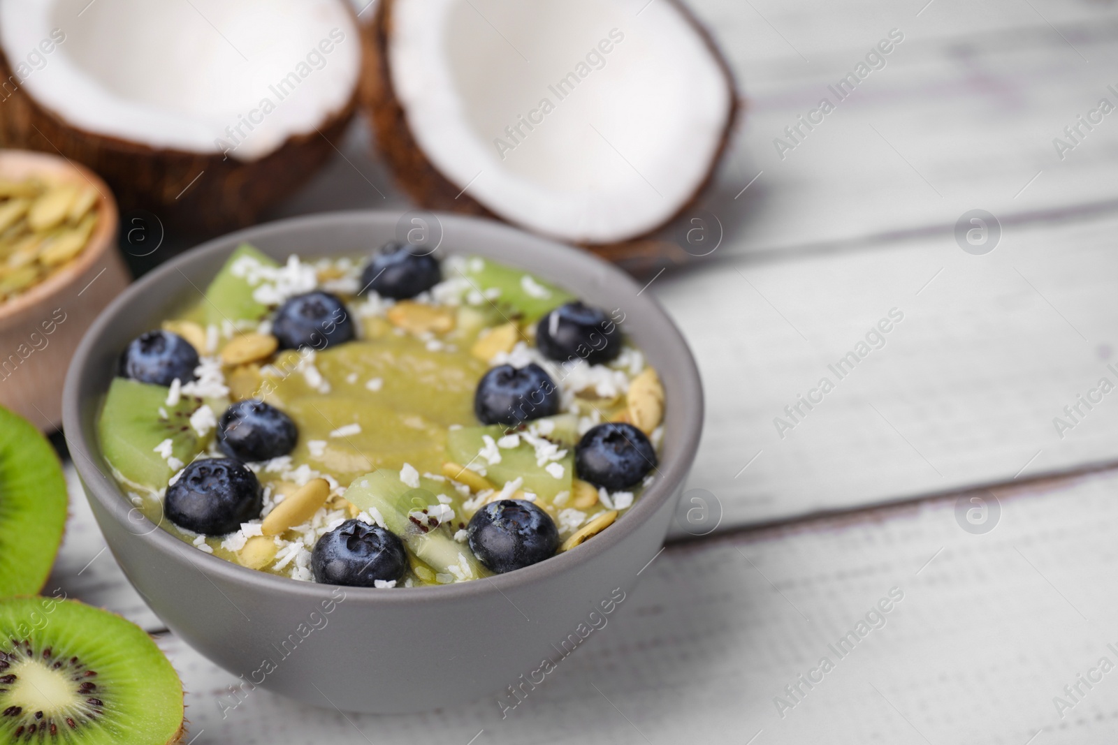 Photo of Bowl of delicious fruit smoothie with fresh blueberries, kiwi slices and coconut flakes on white wooden table, closeup. Space for text