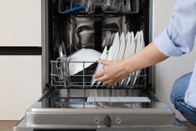 Photo of Woman loading dishwasher with plates indoors, closeup