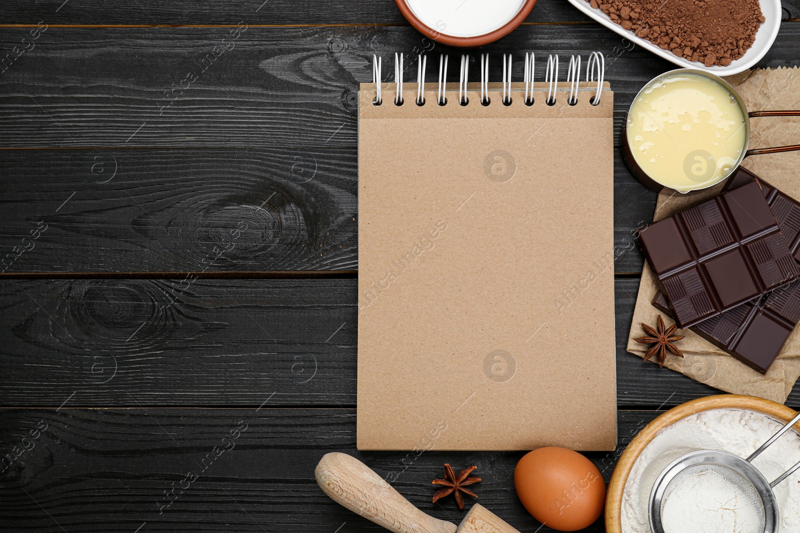 Photo of Blank recipe book and different ingredients on black wooden table, flat lay. Space for text