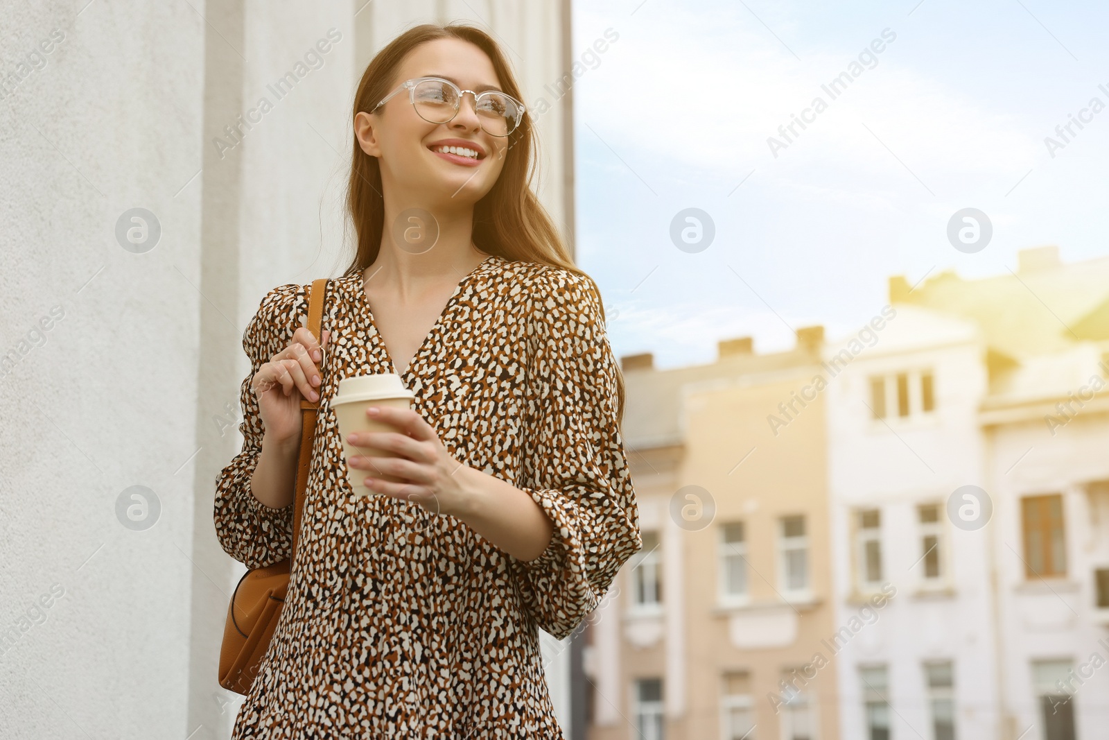 Photo of Young woman with cup of drink walking on city street, space for text