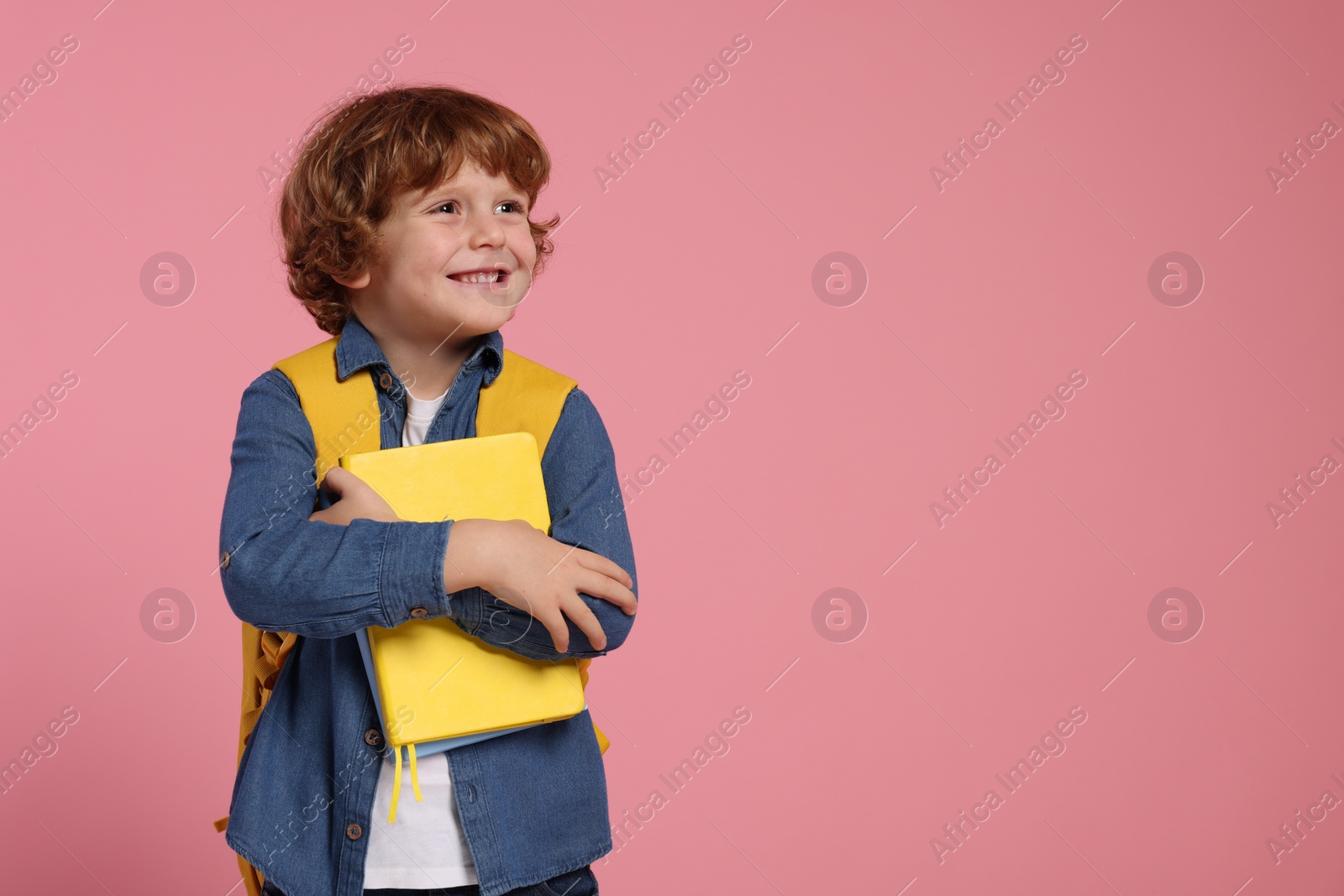 Photo of Happy schoolboy with backpack and books on pink background, space for text