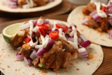 Photo of Delicious tacos with vegetables, meat and sauce on wooden table, closeup