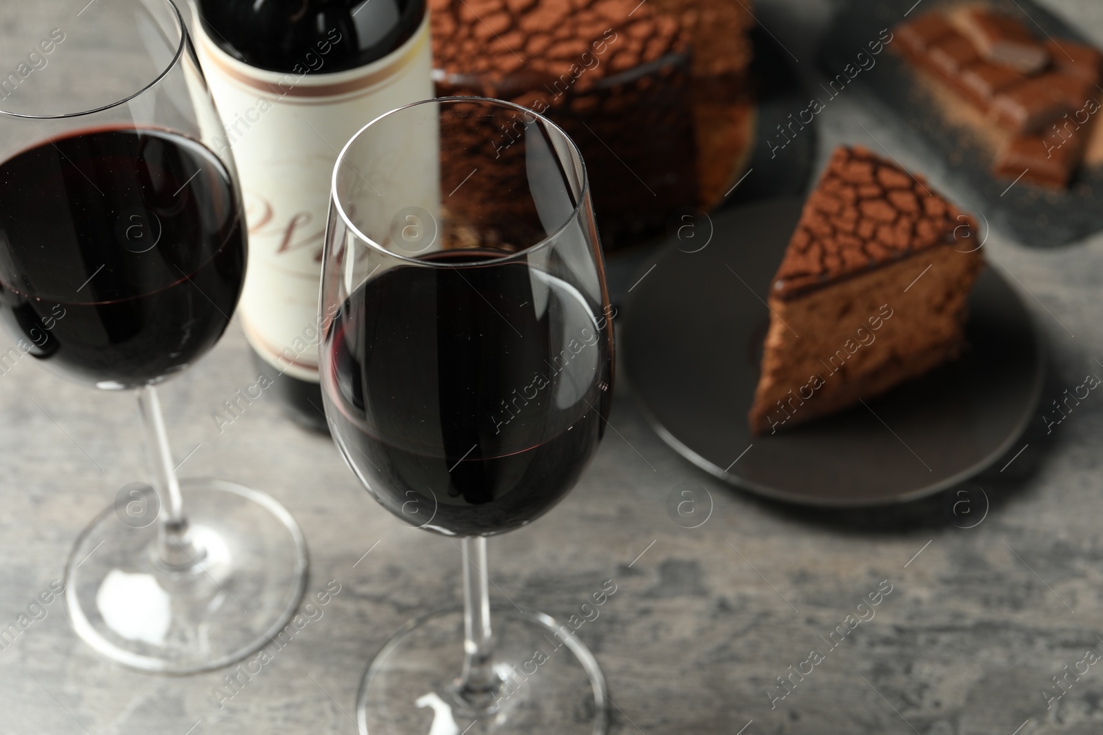 Photo of Delicious chocolate truffle cake and red wine on grey textured table