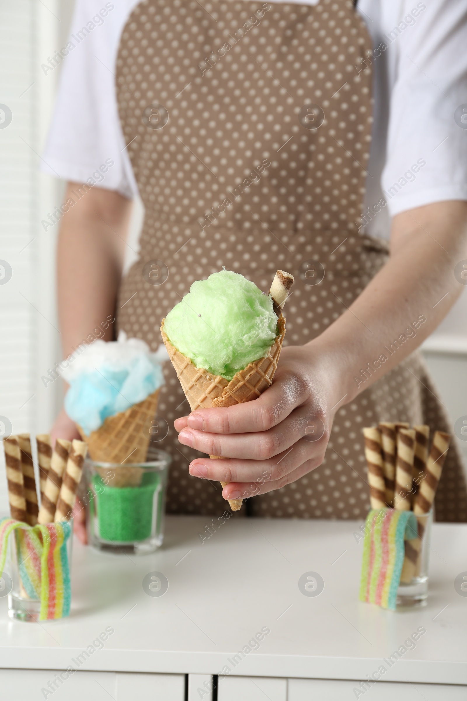 Photo of Woman holding waffle cone with cotton candy indoors, closeup