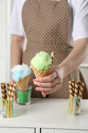 Woman holding waffle cone with cotton candy indoors, closeup