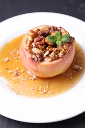 Photo of Tasty baked apple with nuts, honey and mint on gray table, closeup