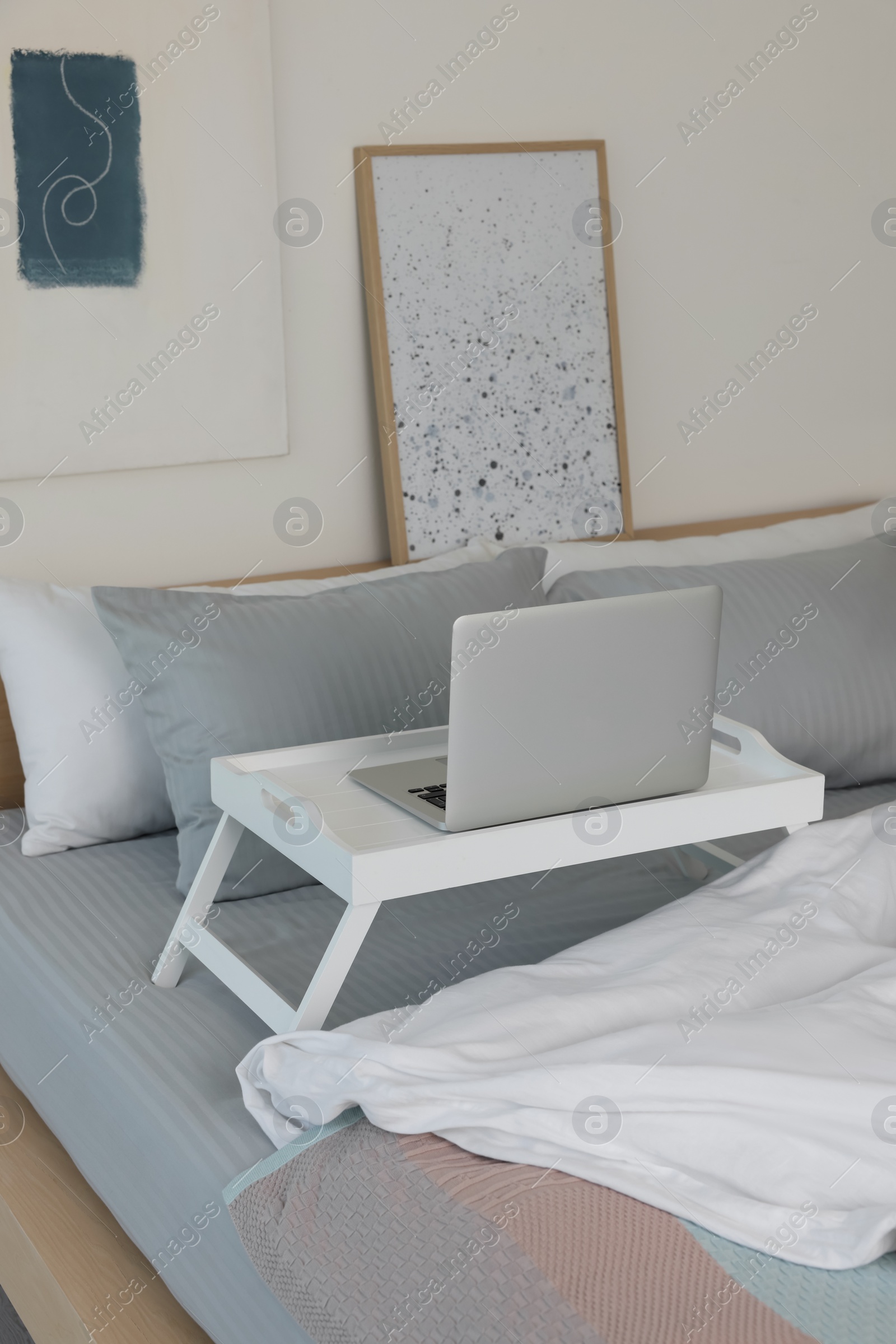 Photo of White tray table with laptop on bed indoors