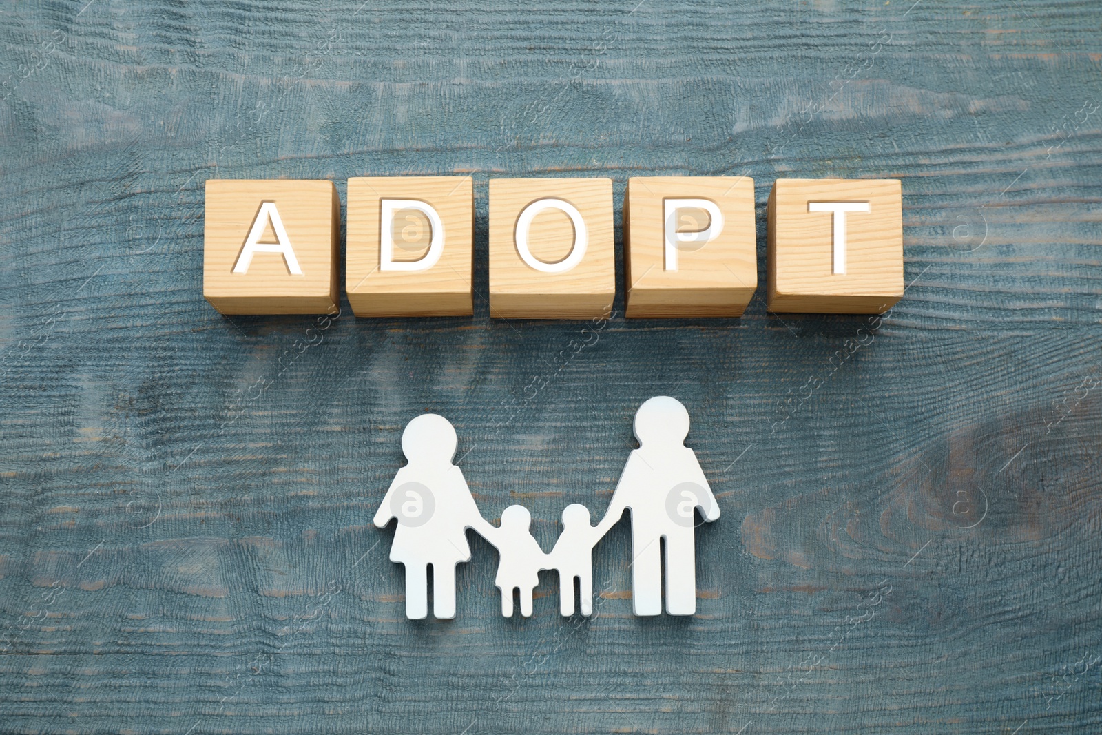 Photo of Family figure and word Adopt made of cubes on blue wooden table, flat lay