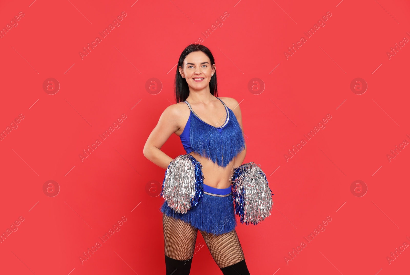 Photo of Beautiful cheerleader in costume holding pom poms on red background