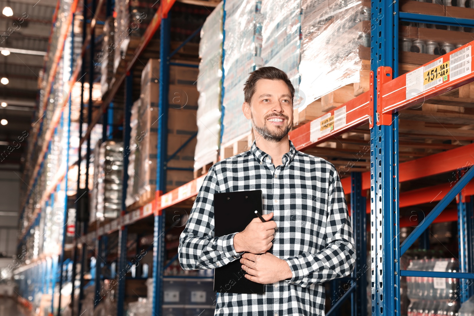 Photo of Happy manager holding clipboard in warehouse with lots of products, low angle view