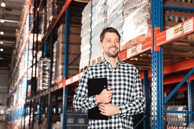 Photo of Happy manager holding clipboard in warehouse with lots of products, low angle view
