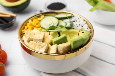 Delicious poke bowl with vegetables, tofu, avocado and microgreens on white tiled table, closeup