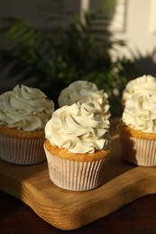 Photo of Tasty cupcakes with vanilla cream on wooden table, closeup