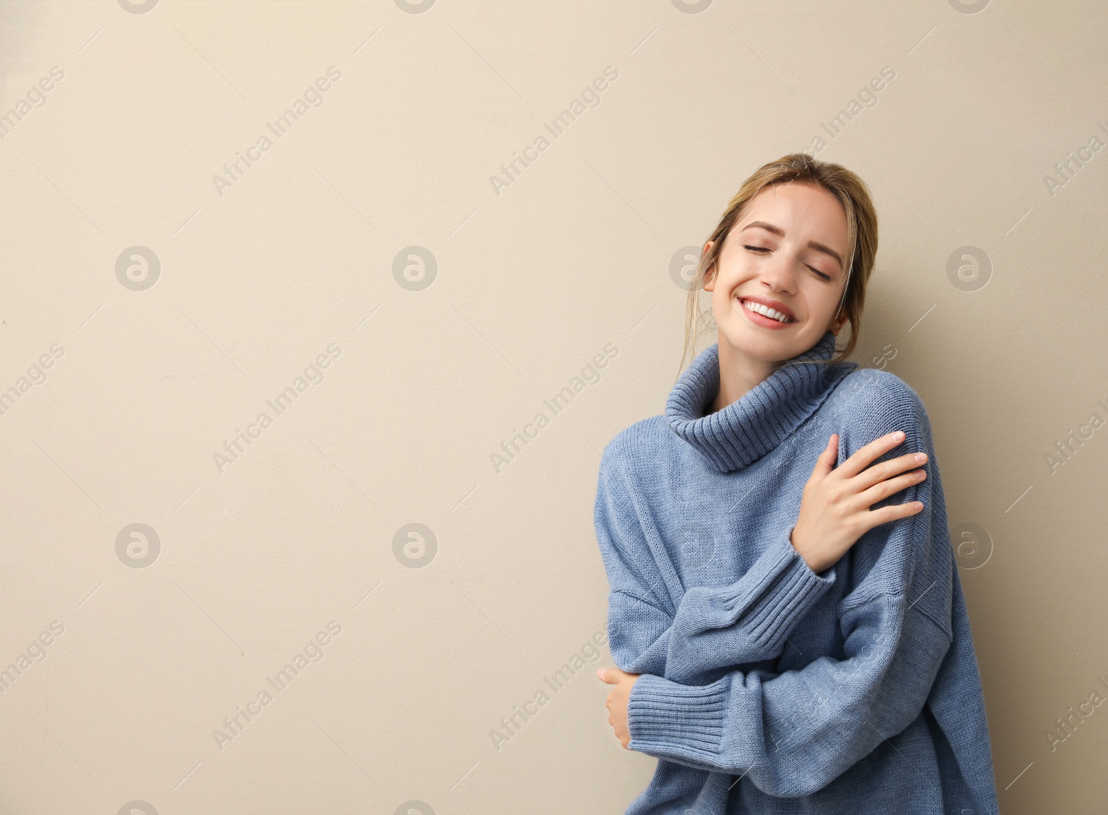 Photo of Beautiful young woman wearing knitted sweater on beige background. Space for text