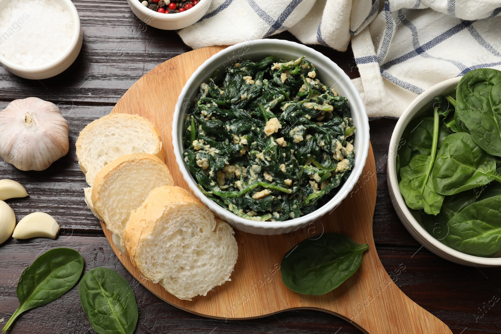 Photo of Tasty spinach dip with egg in bowl, spices and bread on wooden table, top view