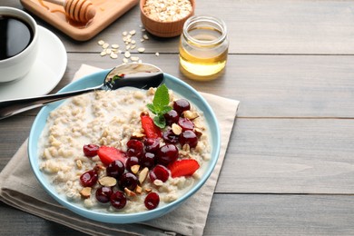 Bowl of oatmeal porridge served with berries on wooden table, space for text