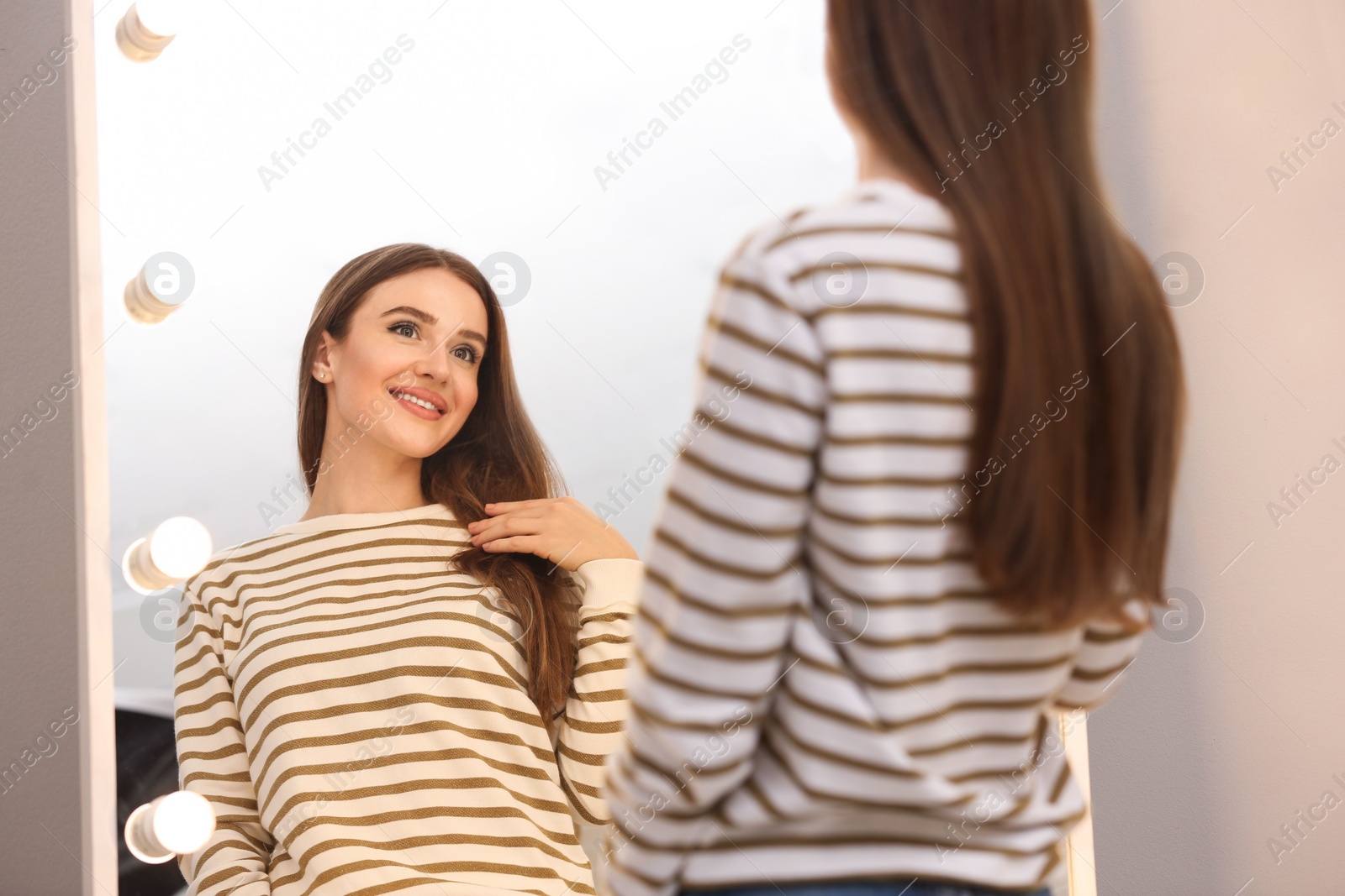 Photo of Beautiful young woman looking at herself in large mirror indoors