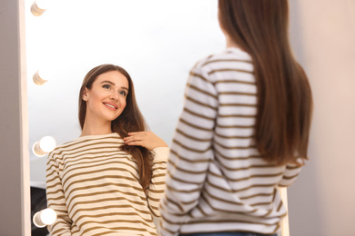 Photo of Beautiful young woman looking at herself in large mirror indoors