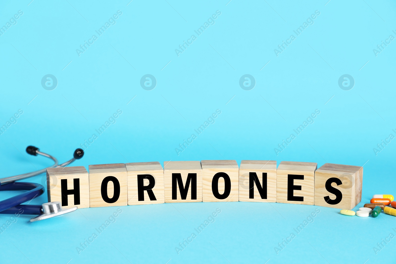 Photo of Word Hormones made of wooden cubes with letters, stethoscope and pills on light blue background