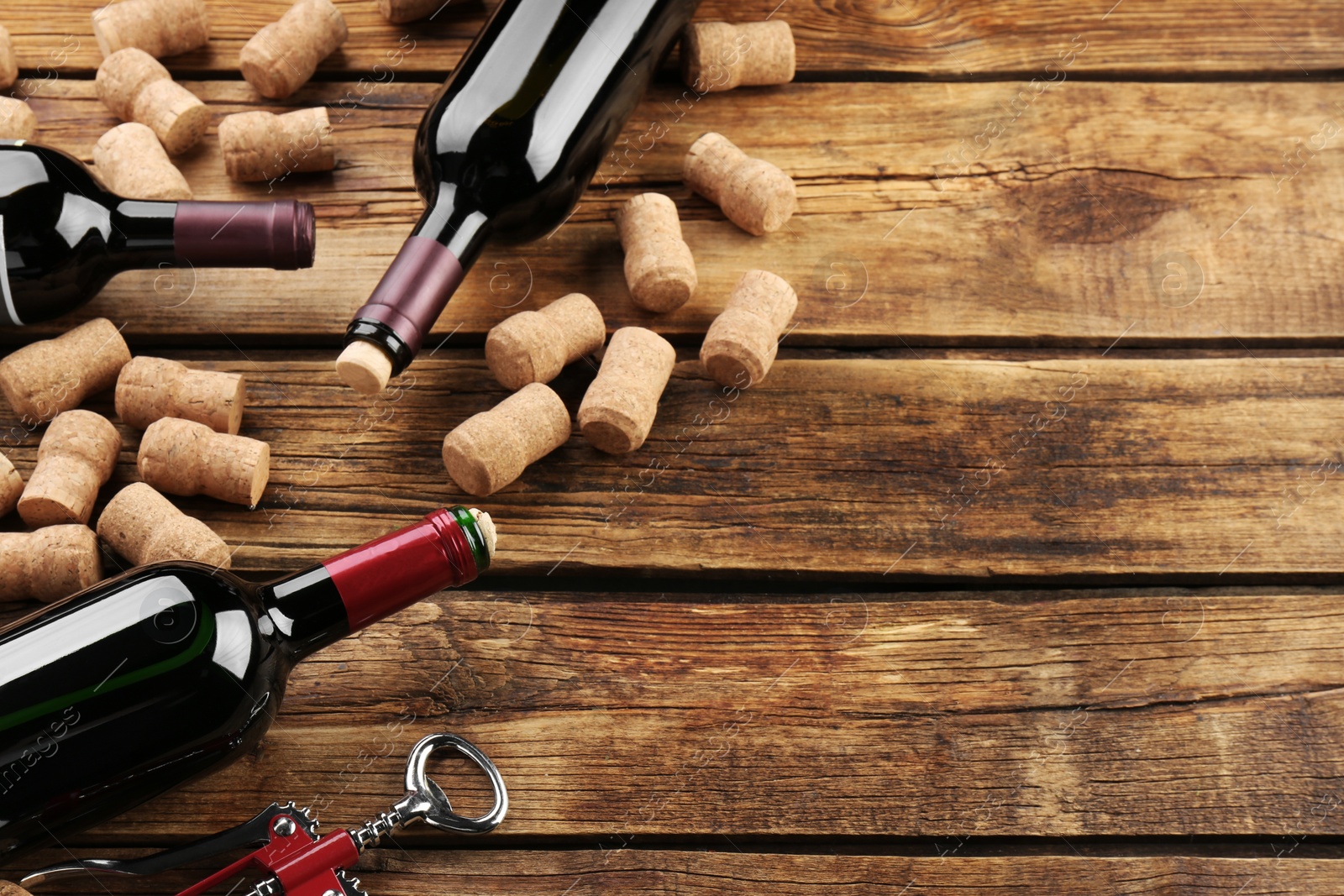 Photo of Bottles with wine, corkscrew and corks on wooden table. Space for text