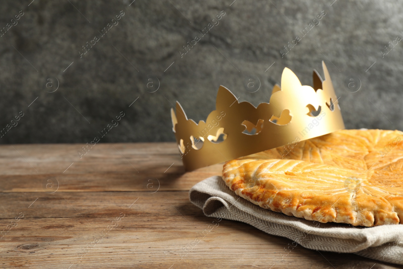 Photo of Traditional galette des Rois with paper crown on wooden table. Space for text