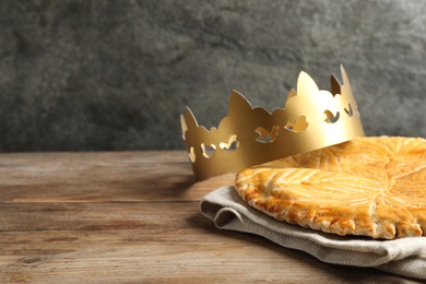 Traditional galette des Rois with paper crown on wooden table. Space for text