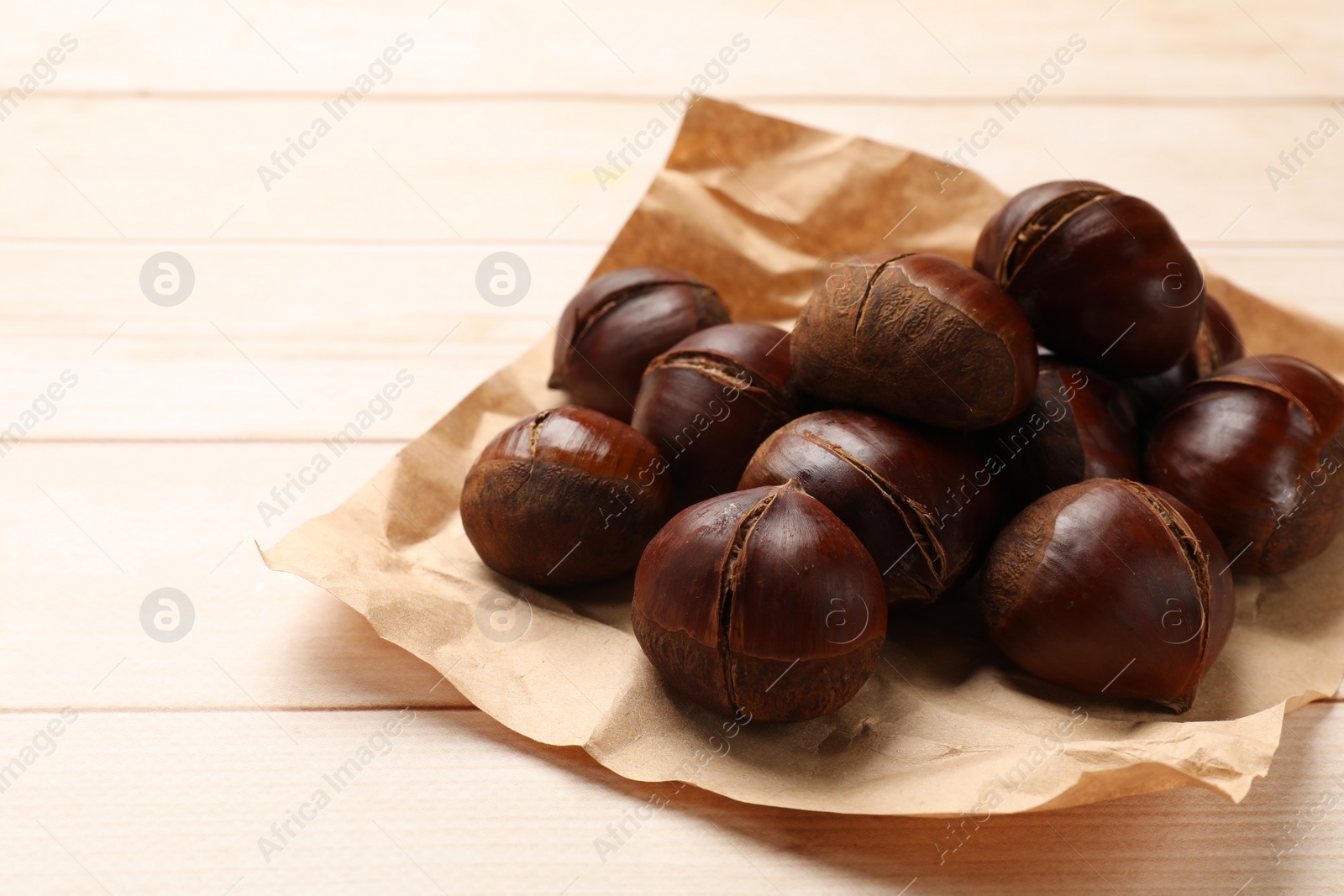 Photo of Roasted edible sweet chestnuts on wooden table, space for text