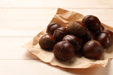 Photo of Roasted edible sweet chestnuts on wooden table, space for text