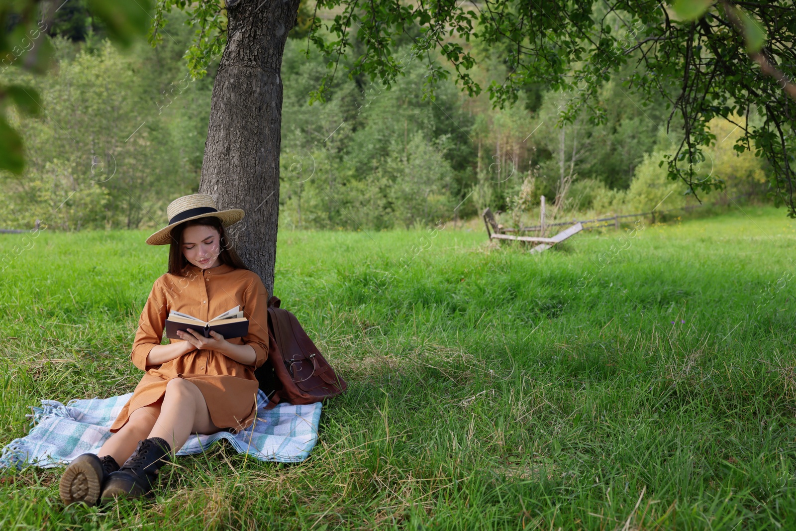 Photo of Young woman reading book under tree on meadow