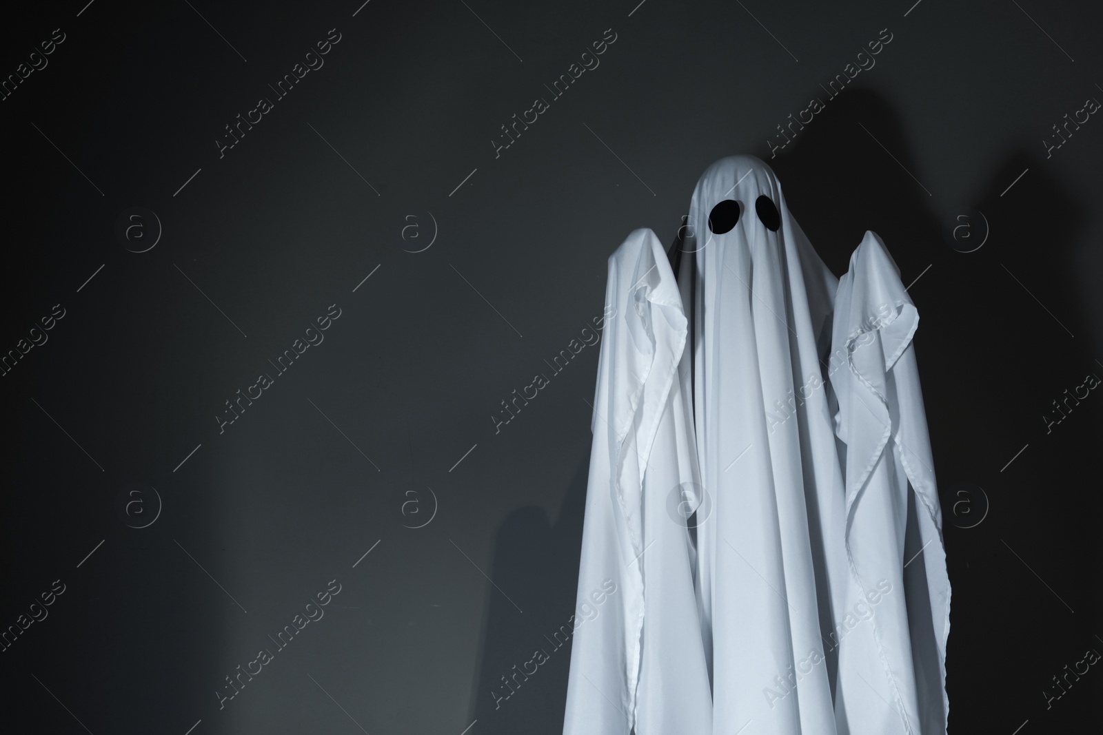 Photo of Creepy ghost. Woman covered by sheet against dark grey background, space for text