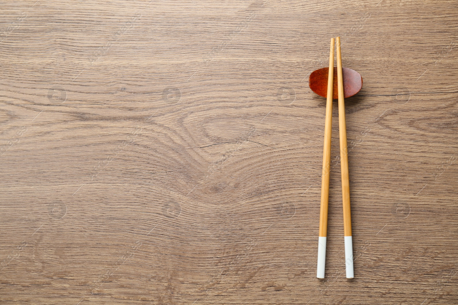 Photo of Pair of chopsticks with rest on wooden table, top view. Space for text