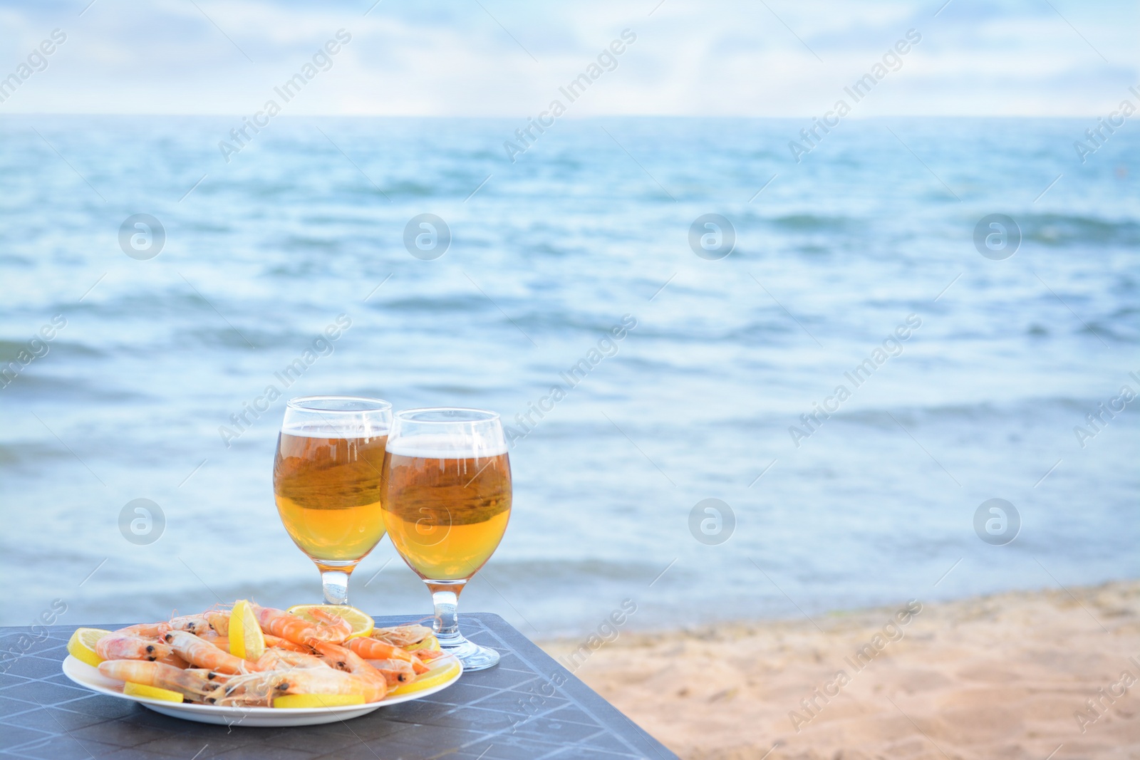 Photo of Cold beer in glasses and shrimps served with lemon on beach