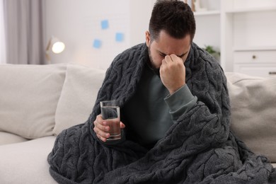 Photo of Man with glass of water suffering from headache on sofa at home