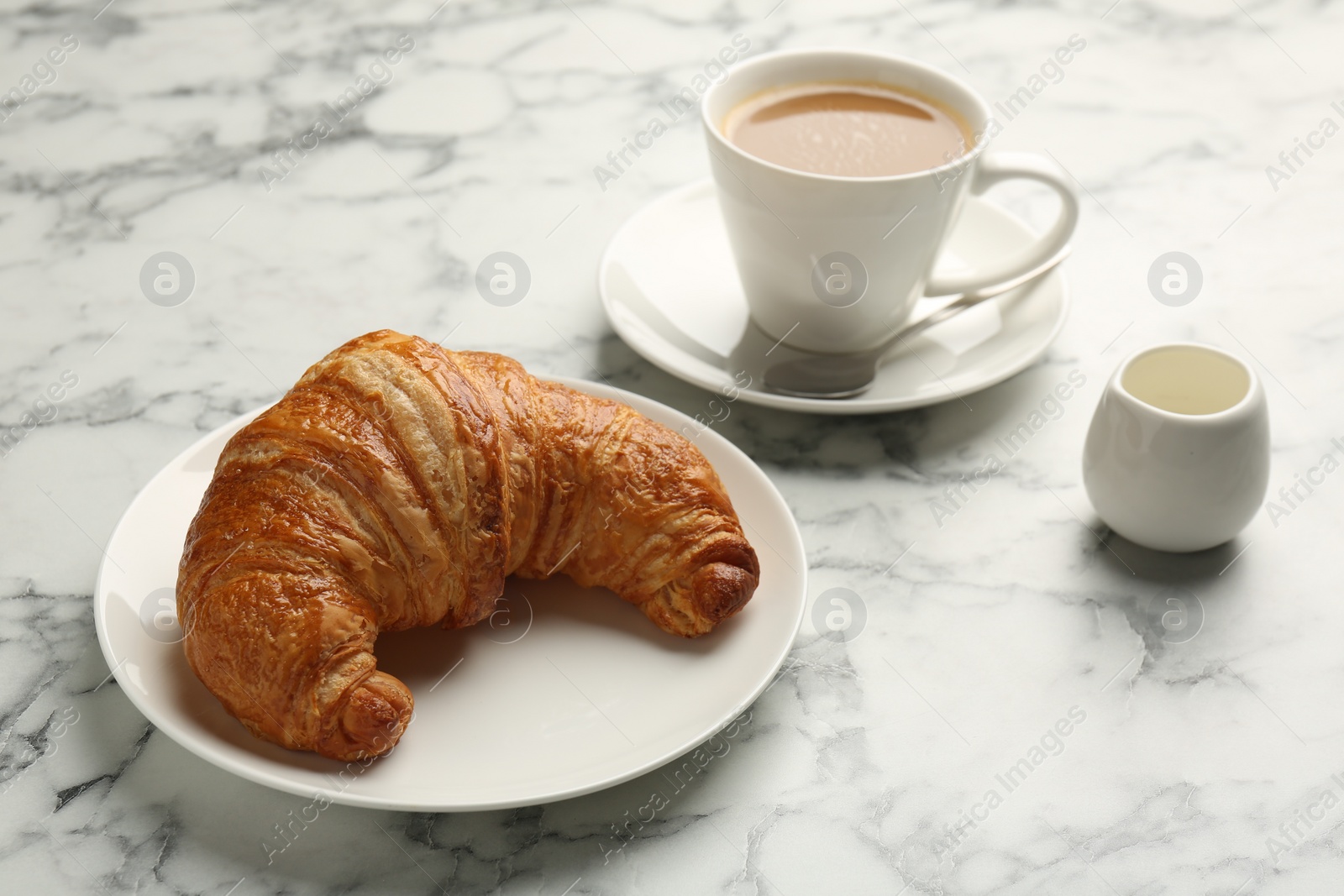 Photo of Delicious fresh croissant and cup of coffee on light marble table